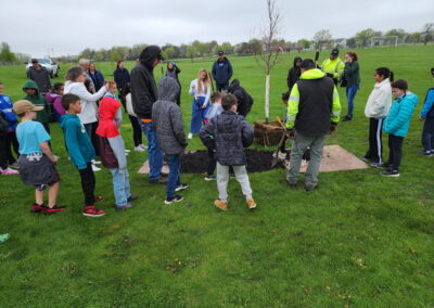 a group of children look on as a tree is planted