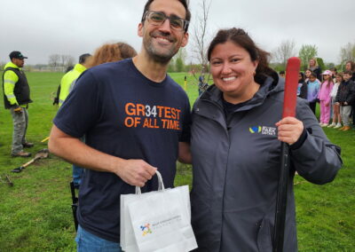 A man holding a bag that has the west chicago parks foundation logo stands next to a woman holding a shovel
